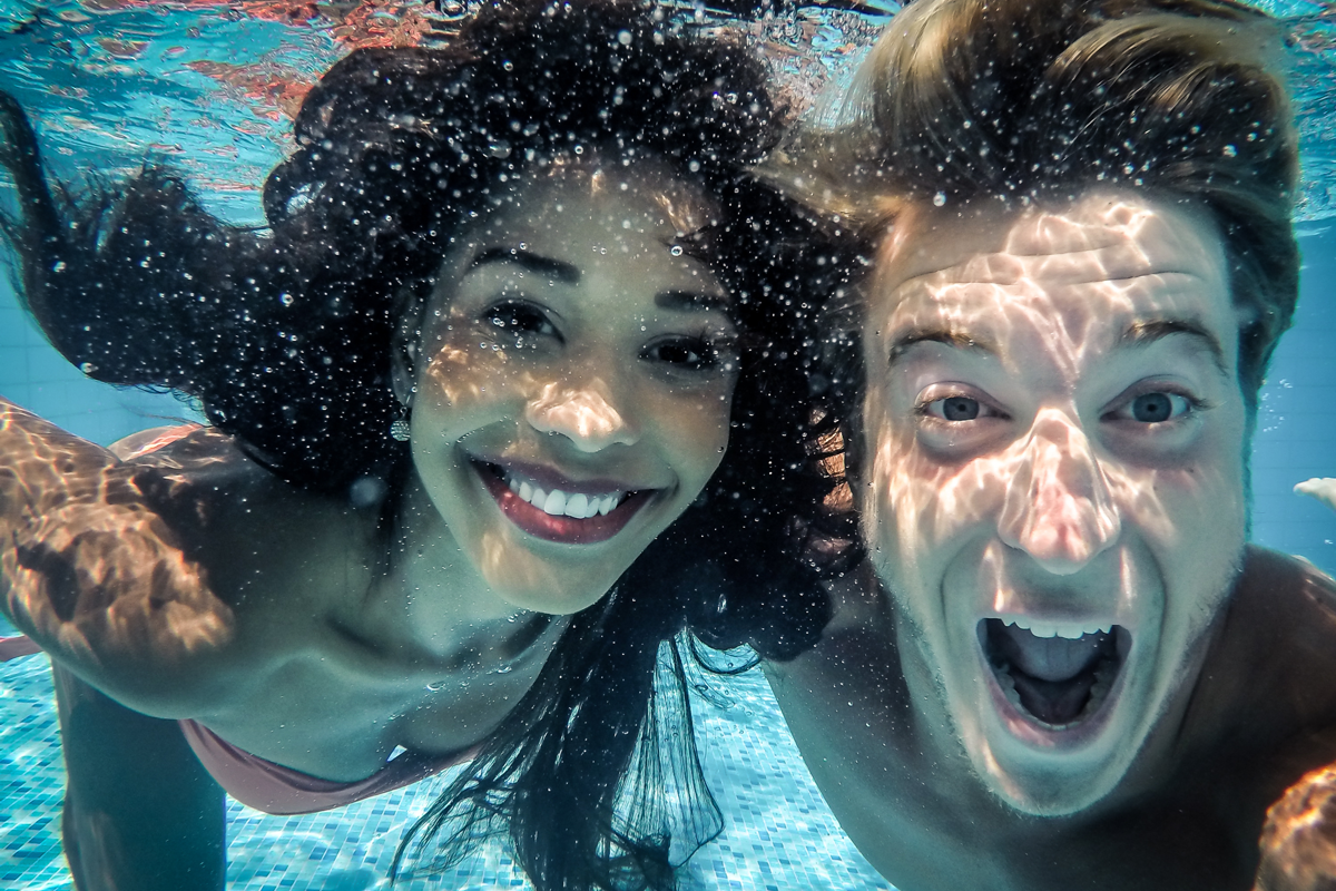 junges Paar lacht in die Kamera unter Wasser im Pool