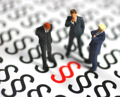 drei Miniaturfiguren in Businesskleidung stehen auf schwarzen Paragraphenzeichen und betrachten ein rotes Paragrapenzeichen