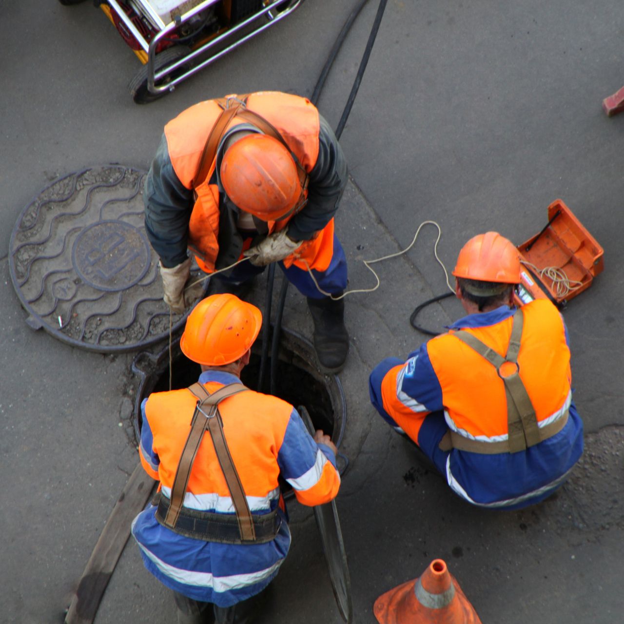 Drei Arbeiter mit Schutzhelmen an geöffnetem Kanaldeckel