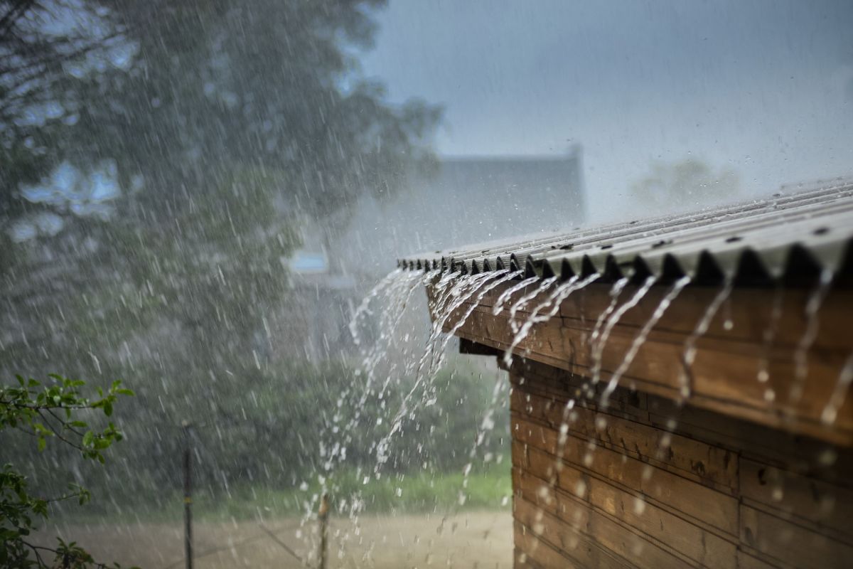 starker Regen prasselt auf das Dach eines Holzhauses, Wasser läuft in Strömen von der Dachkante